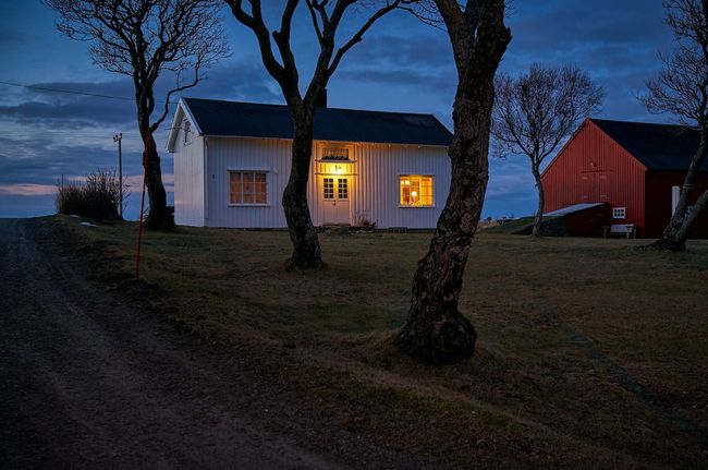Ett vitt hus med svart tak brevid en röd lada i skymningen