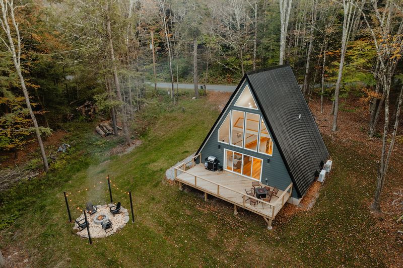 Ett triangelformat hus i en idylisk skogsmiljö med en brasa utanför